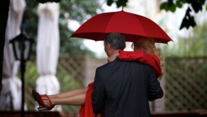 Hochzeitsfoto im Regen - Bräutigam trägt die Braut / Brautpaar mit Schirm von hinten fotografiert